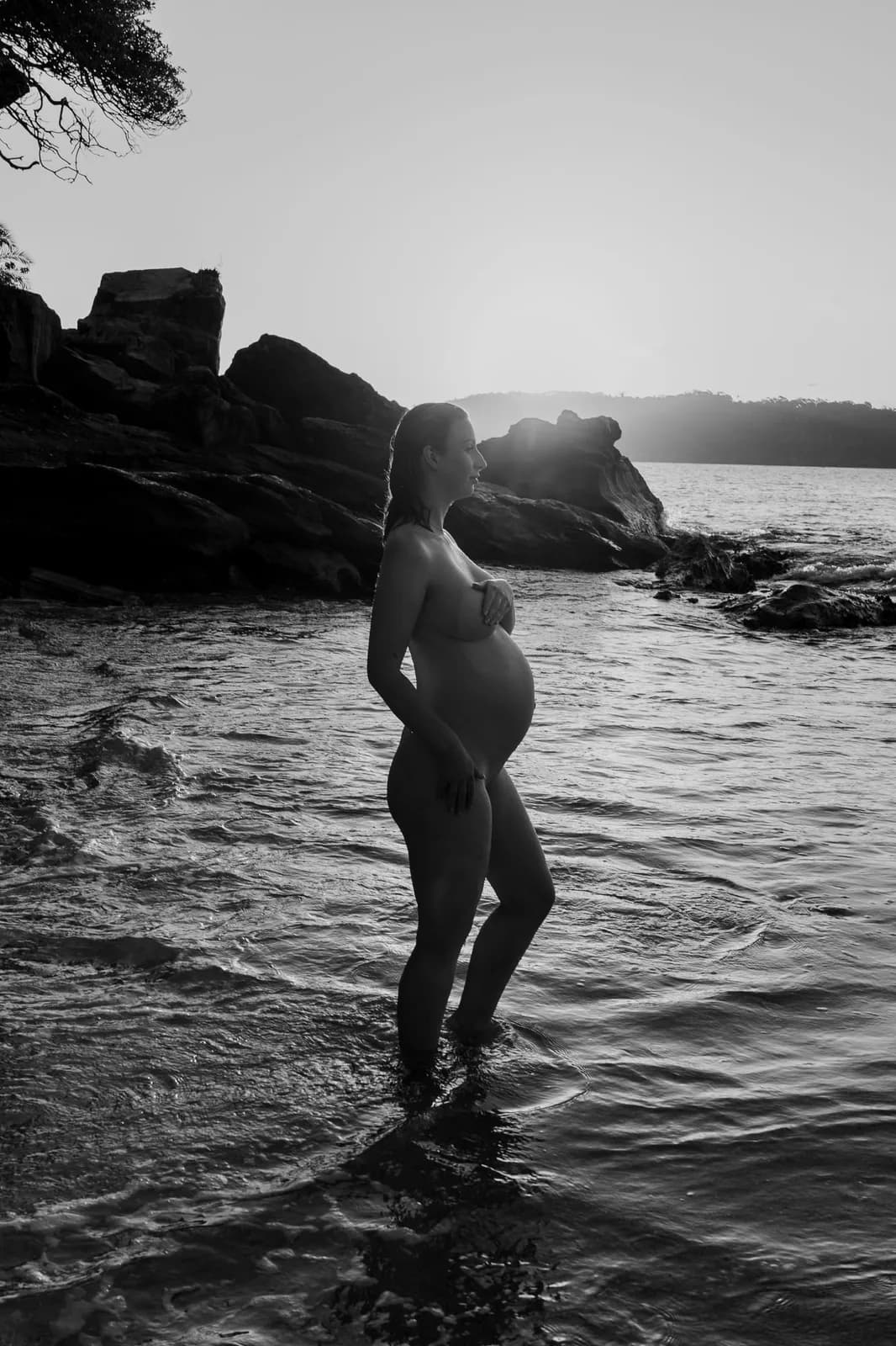 Black and white backlit maternity portrait of an expectant mother standing in the water