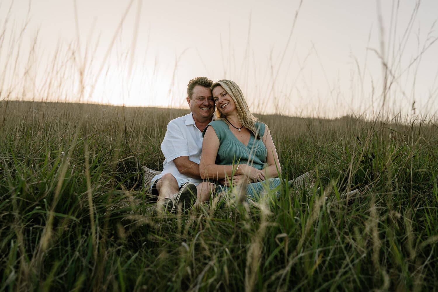 Couple seated together in long grass at golden hour