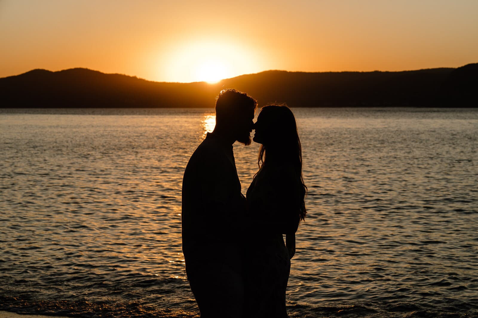 Couple silhouetted against the sunset over the water on a Sydney couples shoot