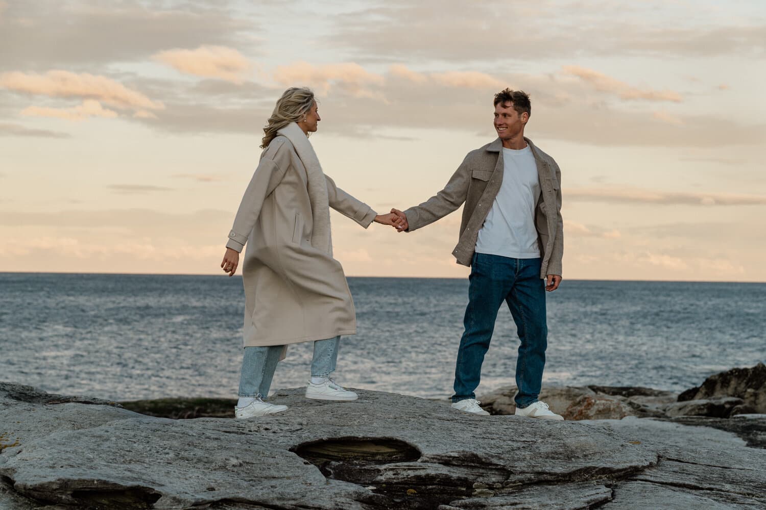Couple holding hands on the sandstone rocks above the harbour