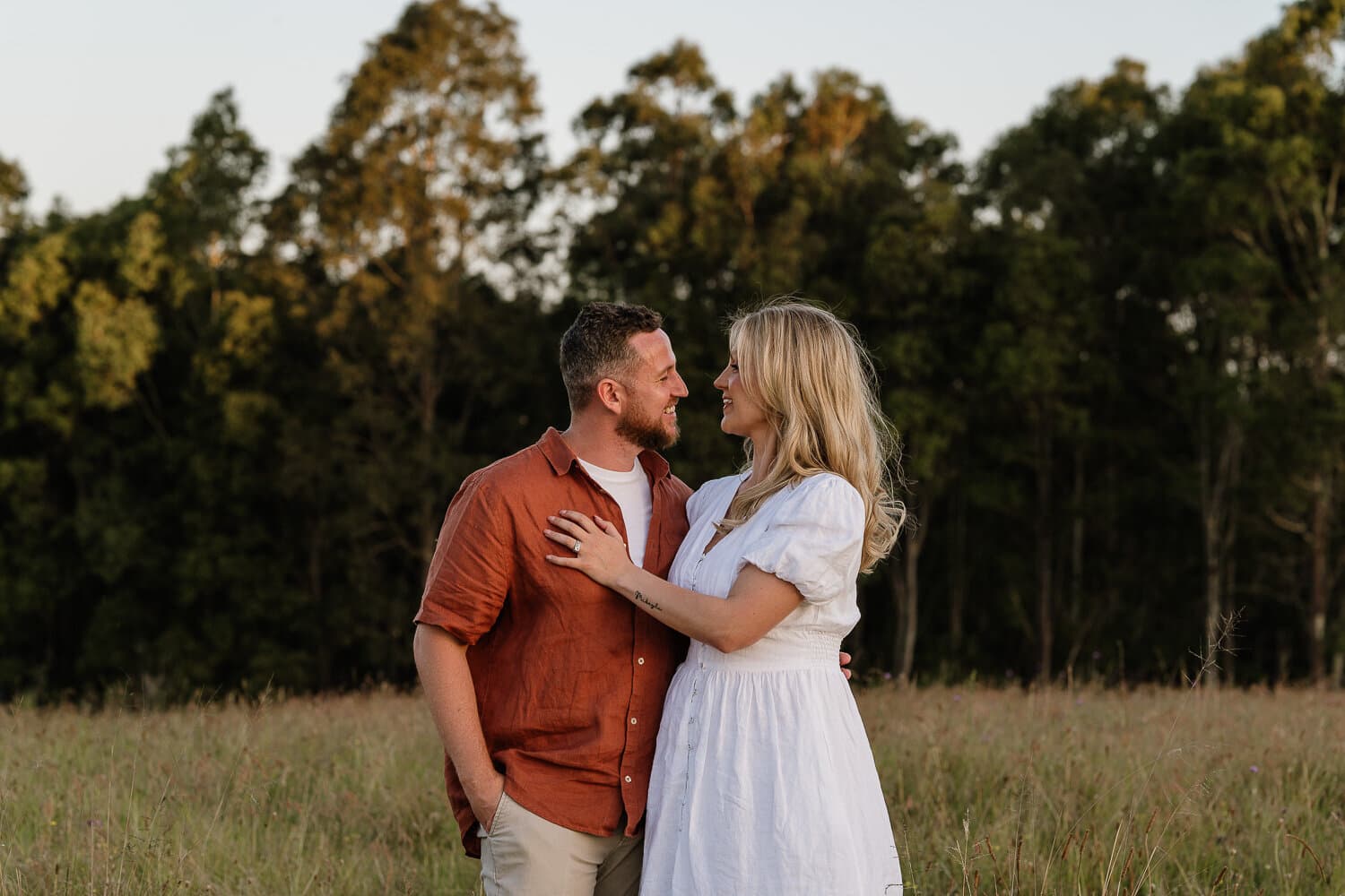 Couple standing together in a paddock at the treeline