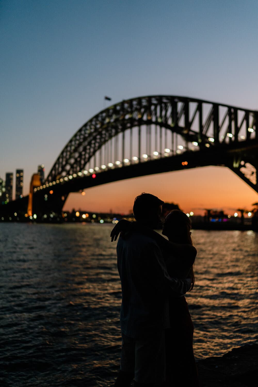 Couple embracing beneath the Sydney Harbour Bridge at dusk