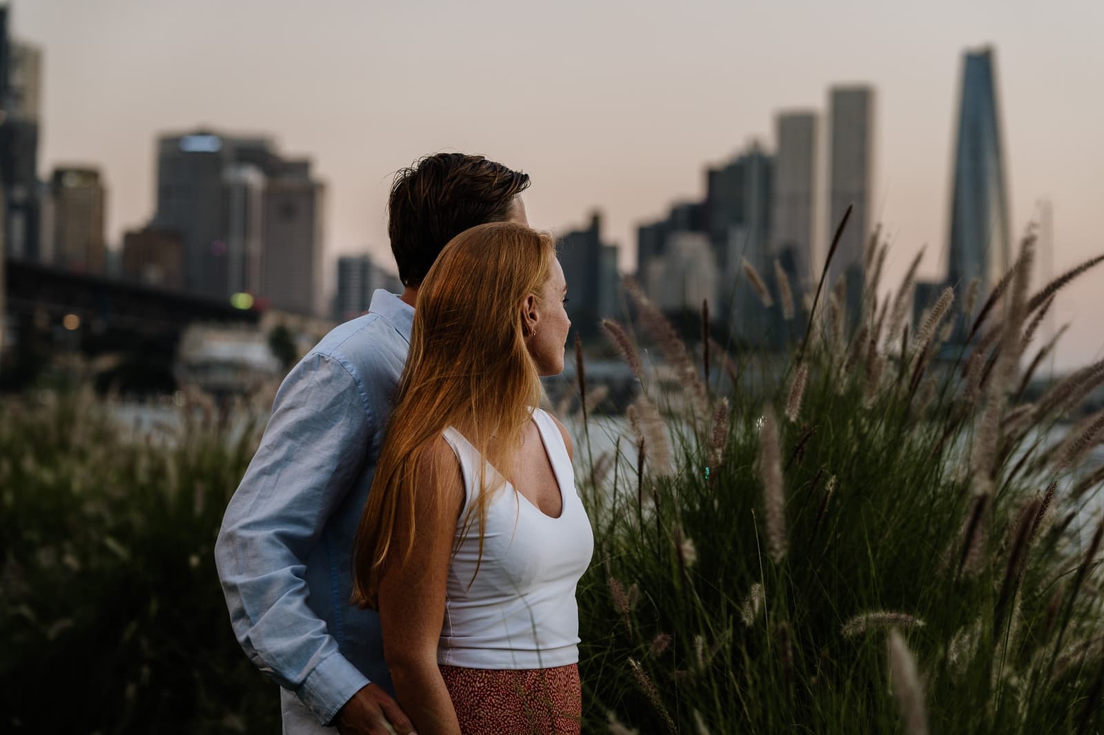 Couple in the long grass with the Sydney city skyline behind them