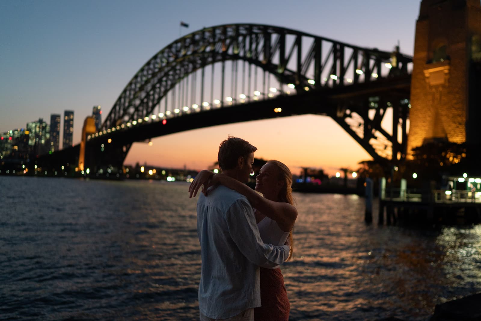 Couple together beneath the Sydney Harbour Bridge as the lights come on