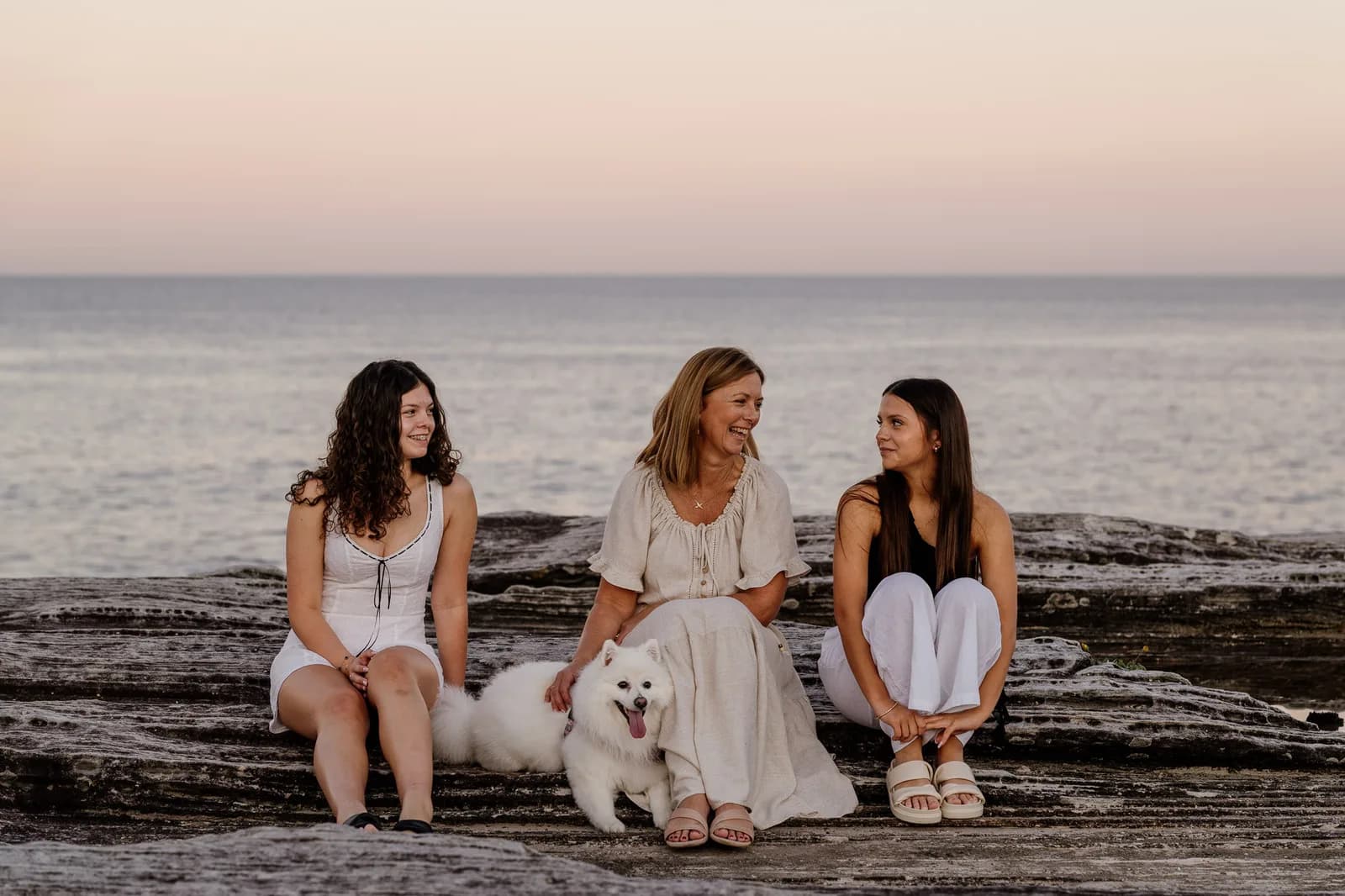 Family seated on a coastal rock shelf under a pastel evening sky