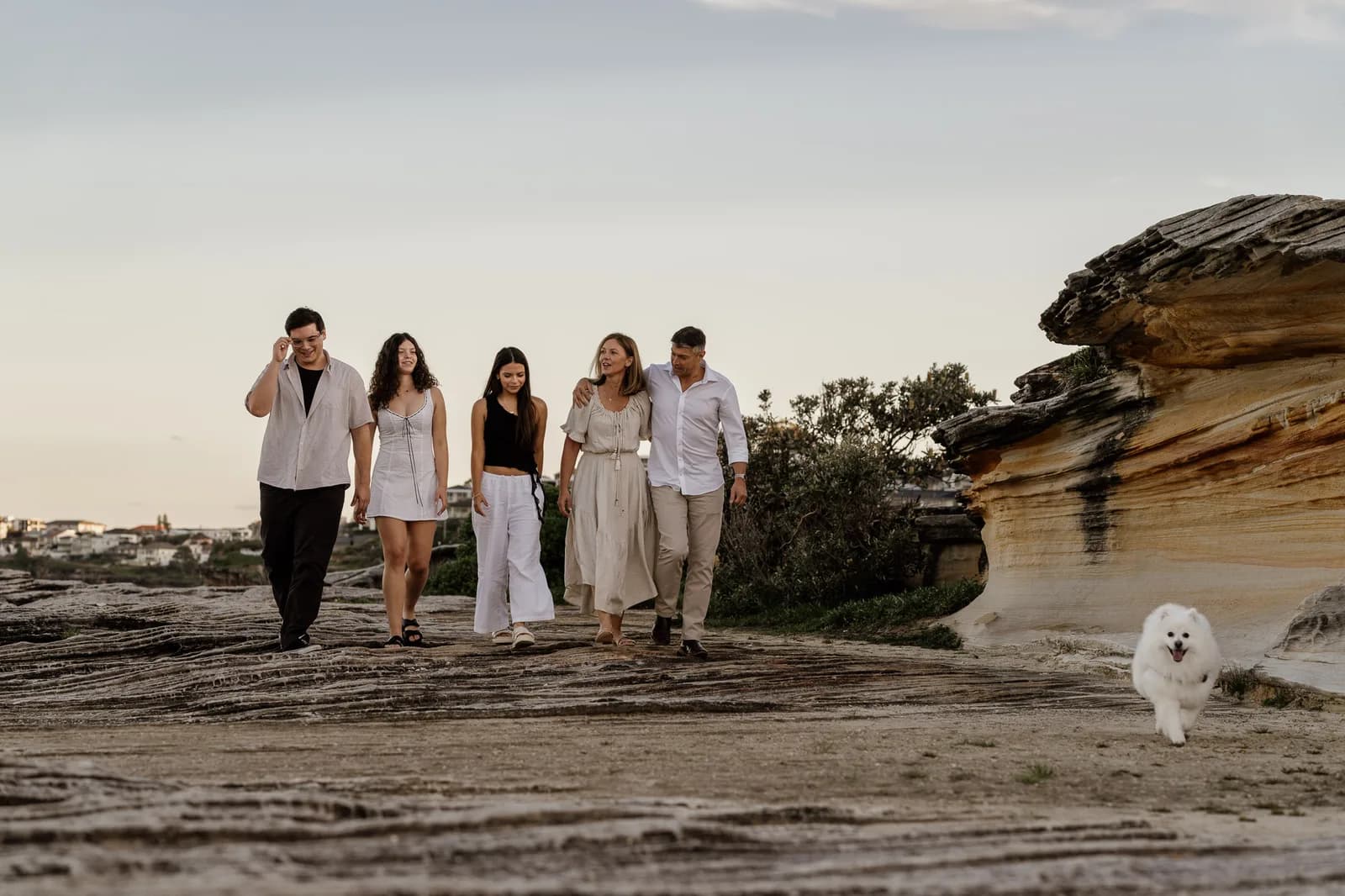 Family walking a coastal rock shelf at sunset with their dog