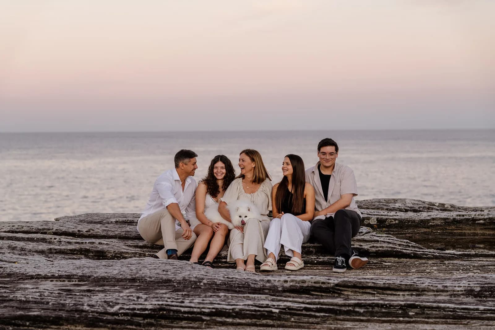 Family seated together on the rocks with the ocean behind them