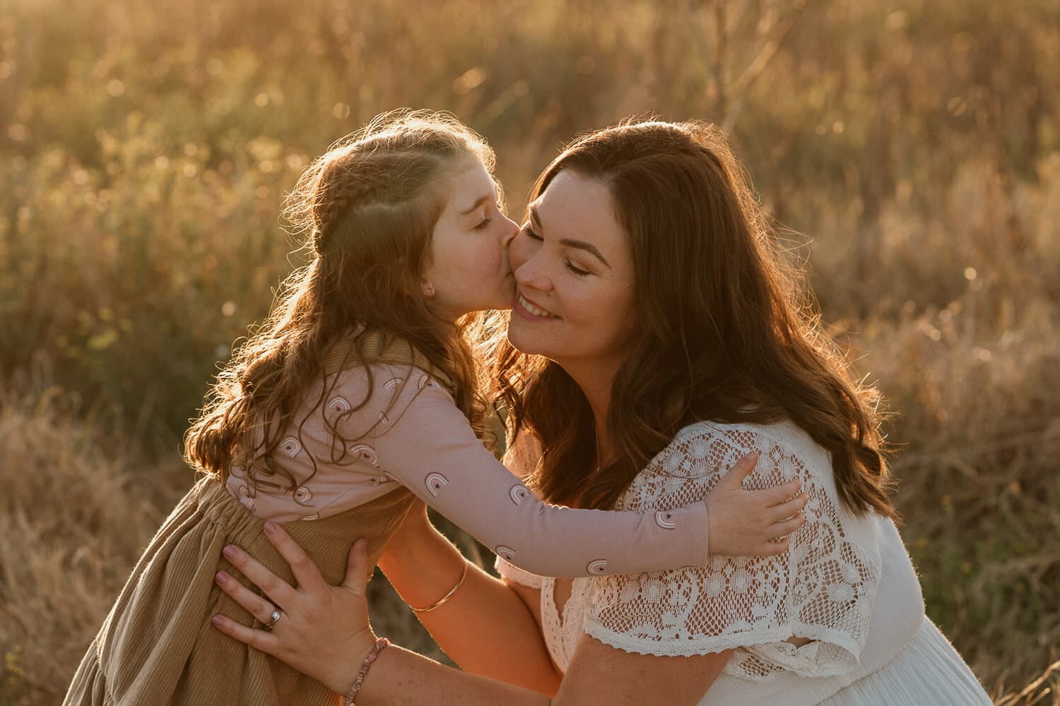 Mother and daughter embracing in tall grass at sunset