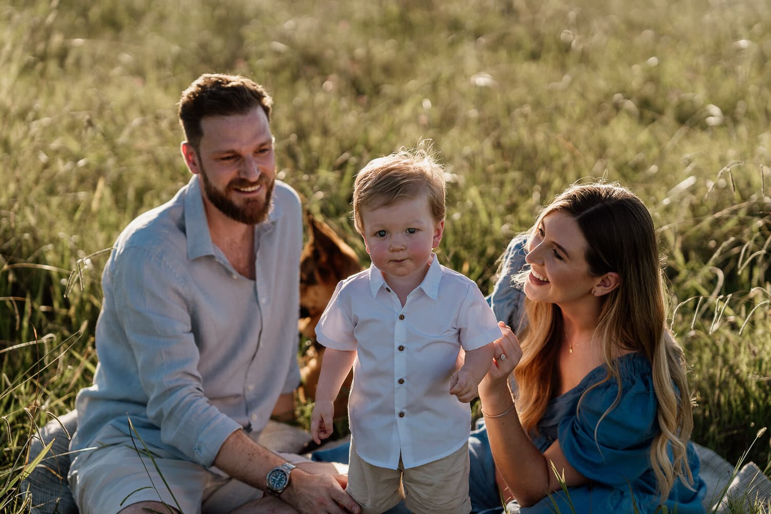 Parents seated in long grass with their young son during a Sydney family photoshoot