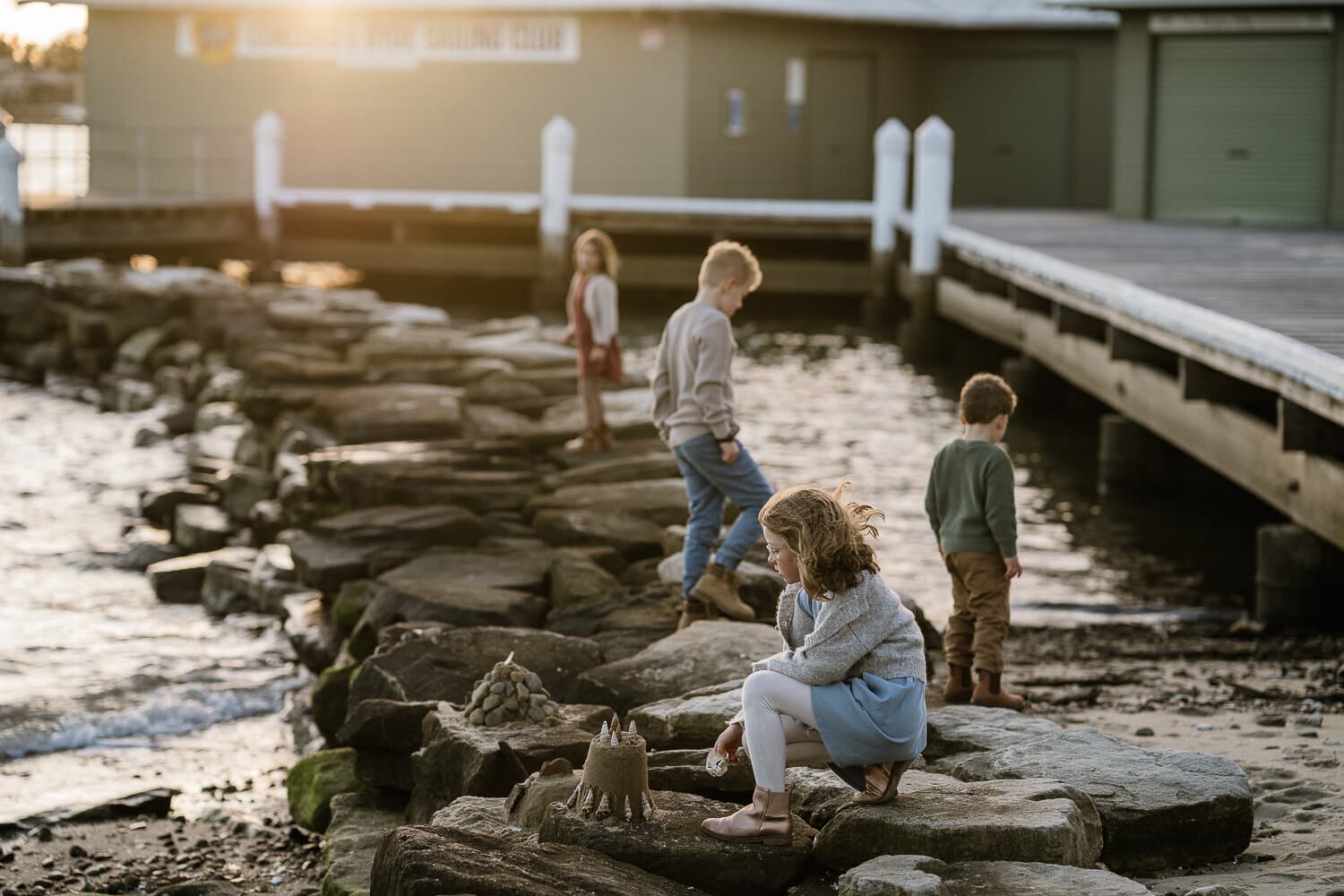 Children exploring the rocks by a Sydney jetty at dusk