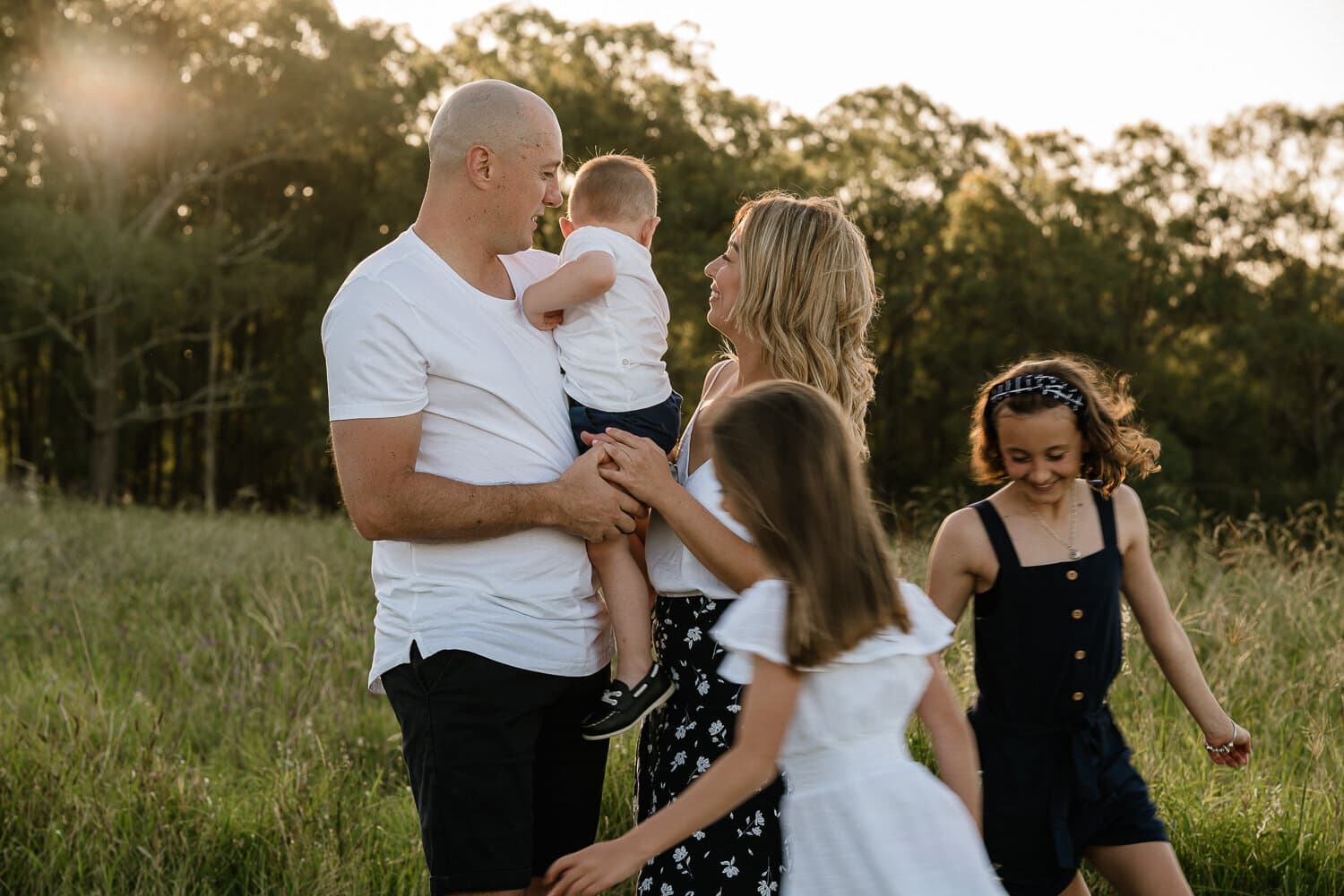 Parents and their 3 children standing together in a paddock at sunset