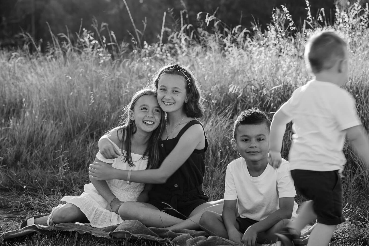 Black and white frame of siblings sitting together in long grass