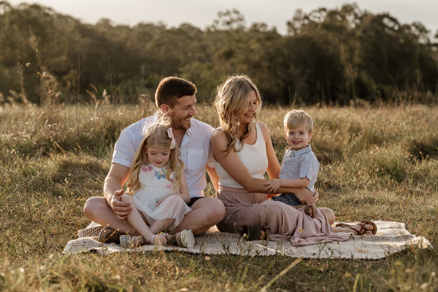 Family on a picnic rug in a paddock at golden hour
