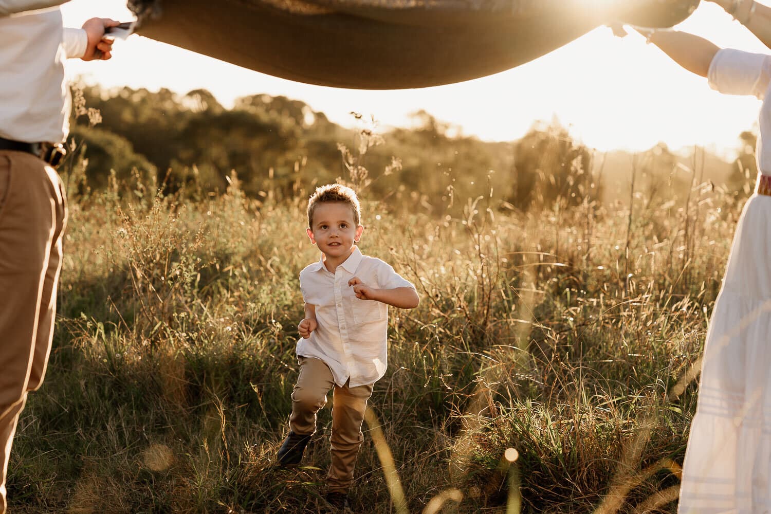 Young boy under a blanket held up to the golden light