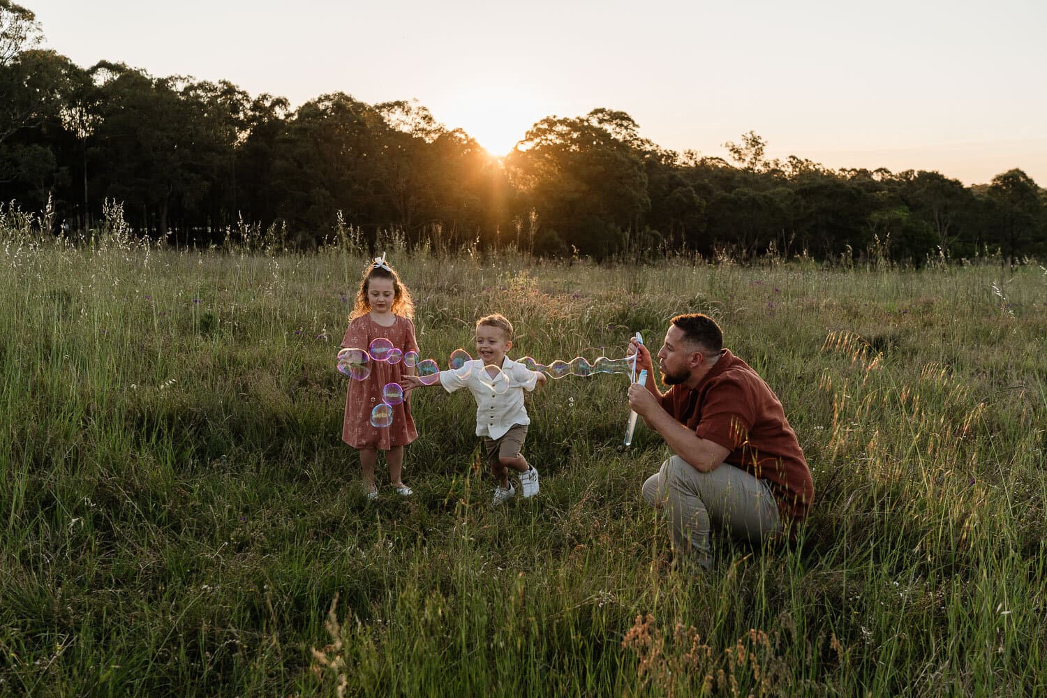 Father photographing his toddler in a field as the sun sets