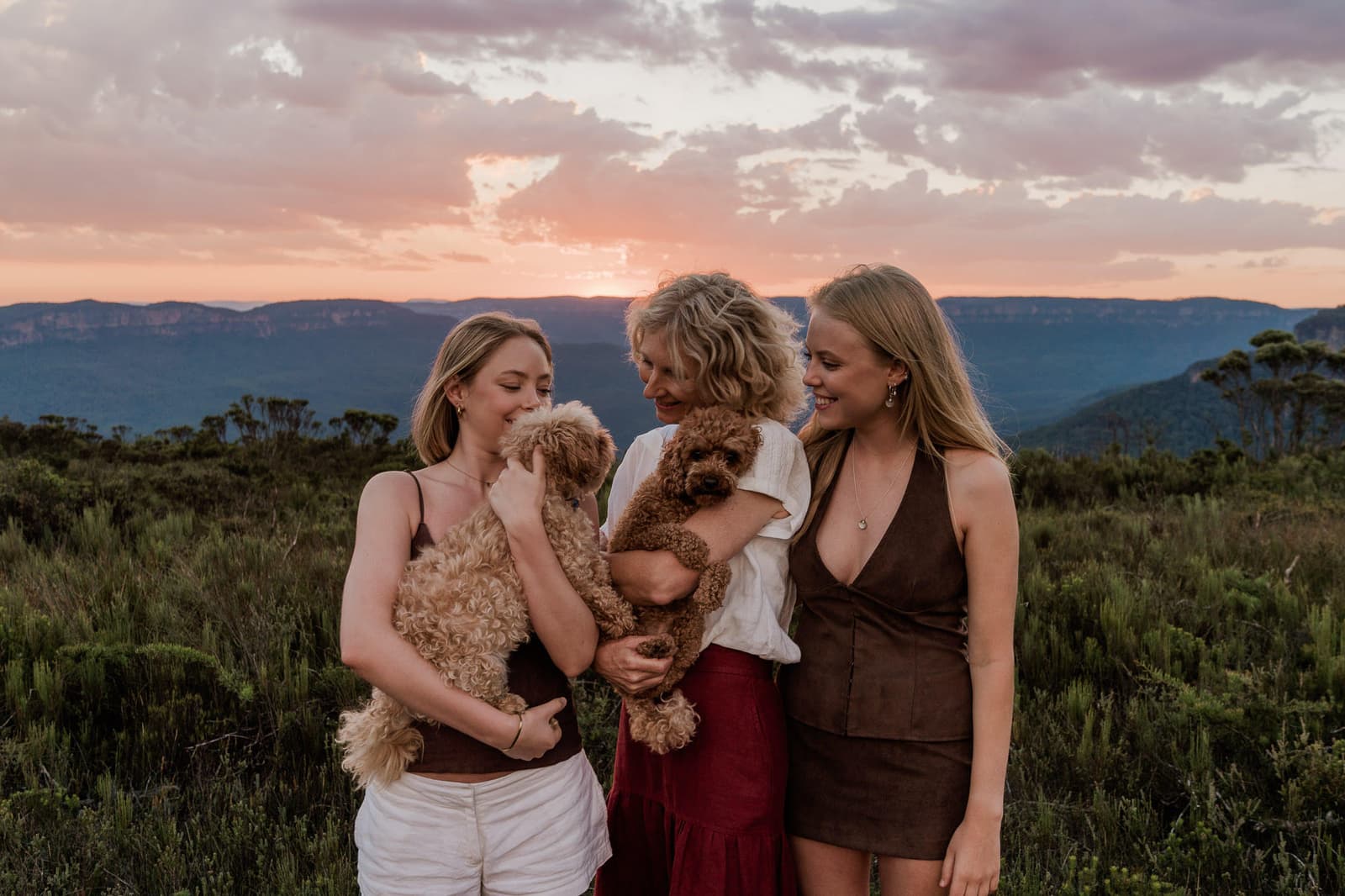 A mother and her 2 daughters holding their cavoodles on a Blue Mountains clifftop at sunset