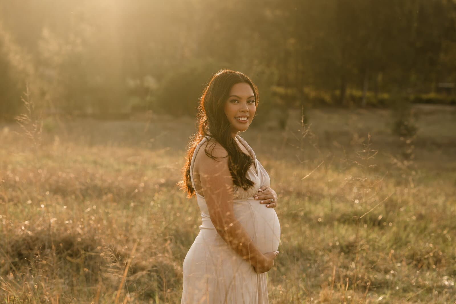 Expectant mother in a flowing gown in a golden paddock at sunset