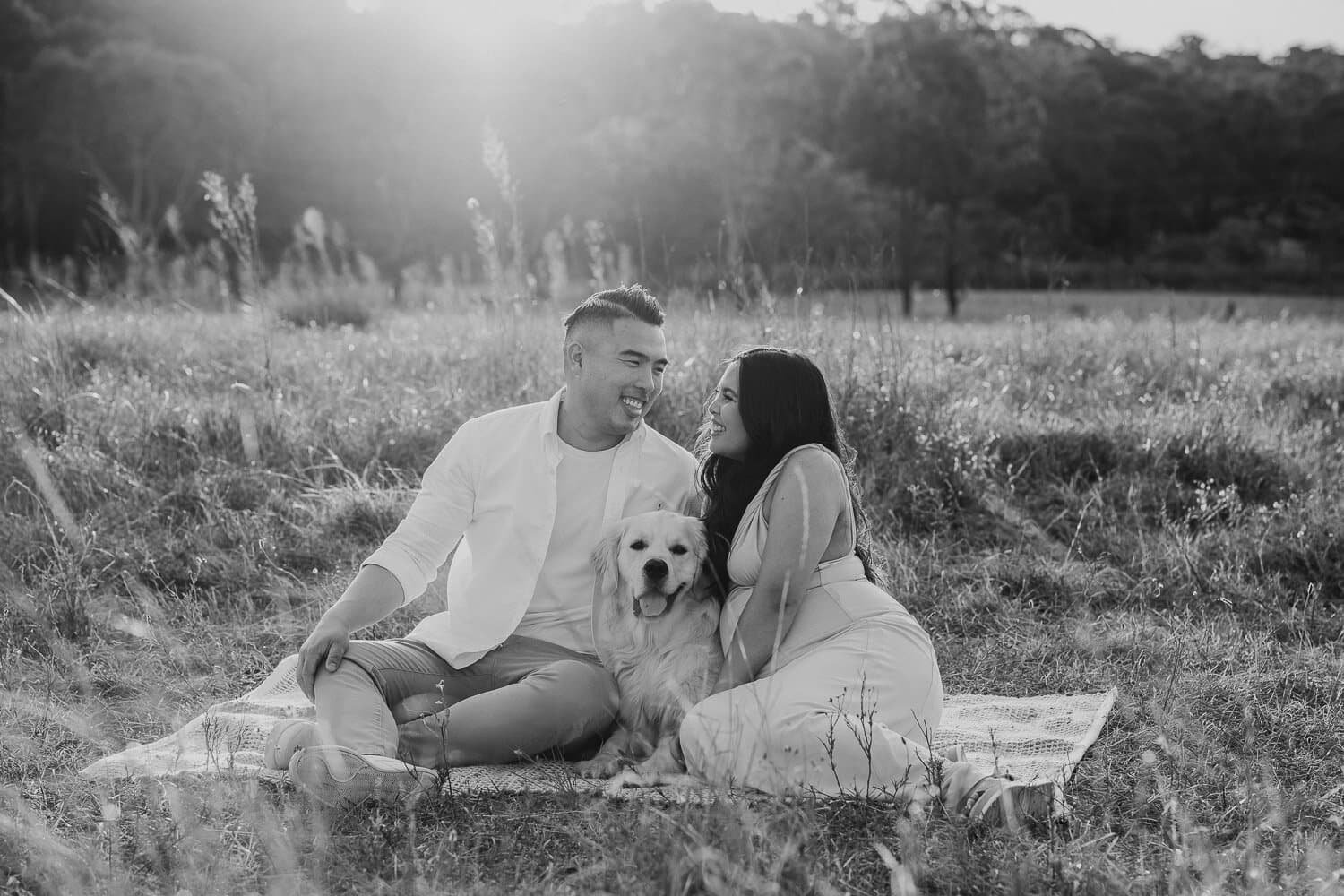 Black and white maternity photograph of a couple and their dog on a picnic blanket