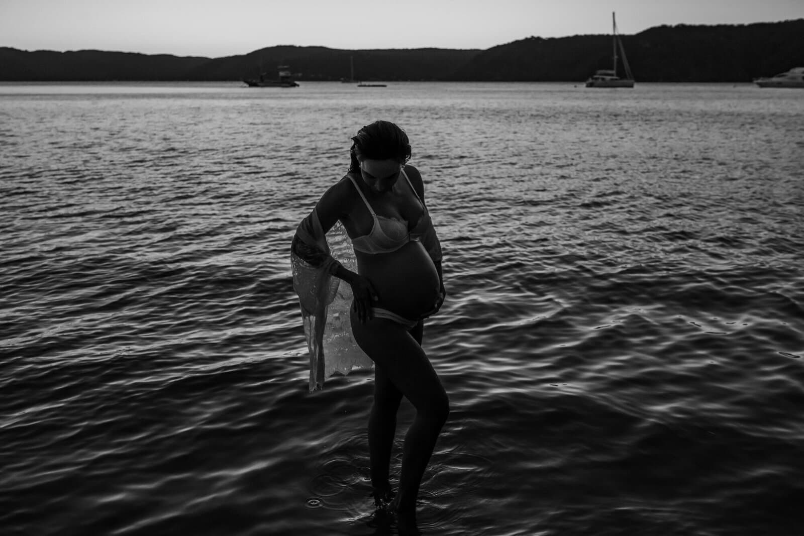 Black and white photograph of an expecting mother wading in open water