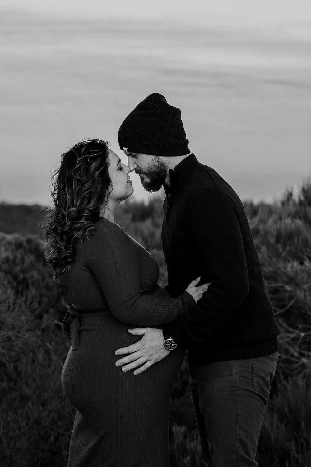 Black and white photograph of an expecting couple with their hands on the baby bump