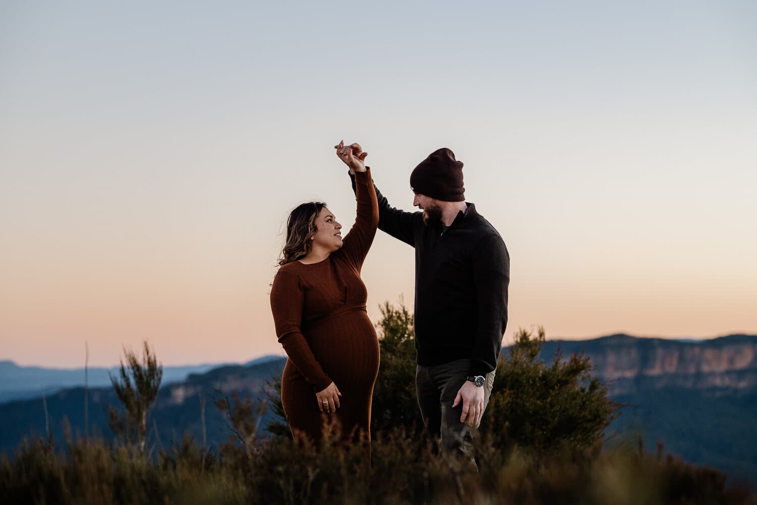 Expecting couple dancing at sunset above a valley on a Sydney maternity shoot