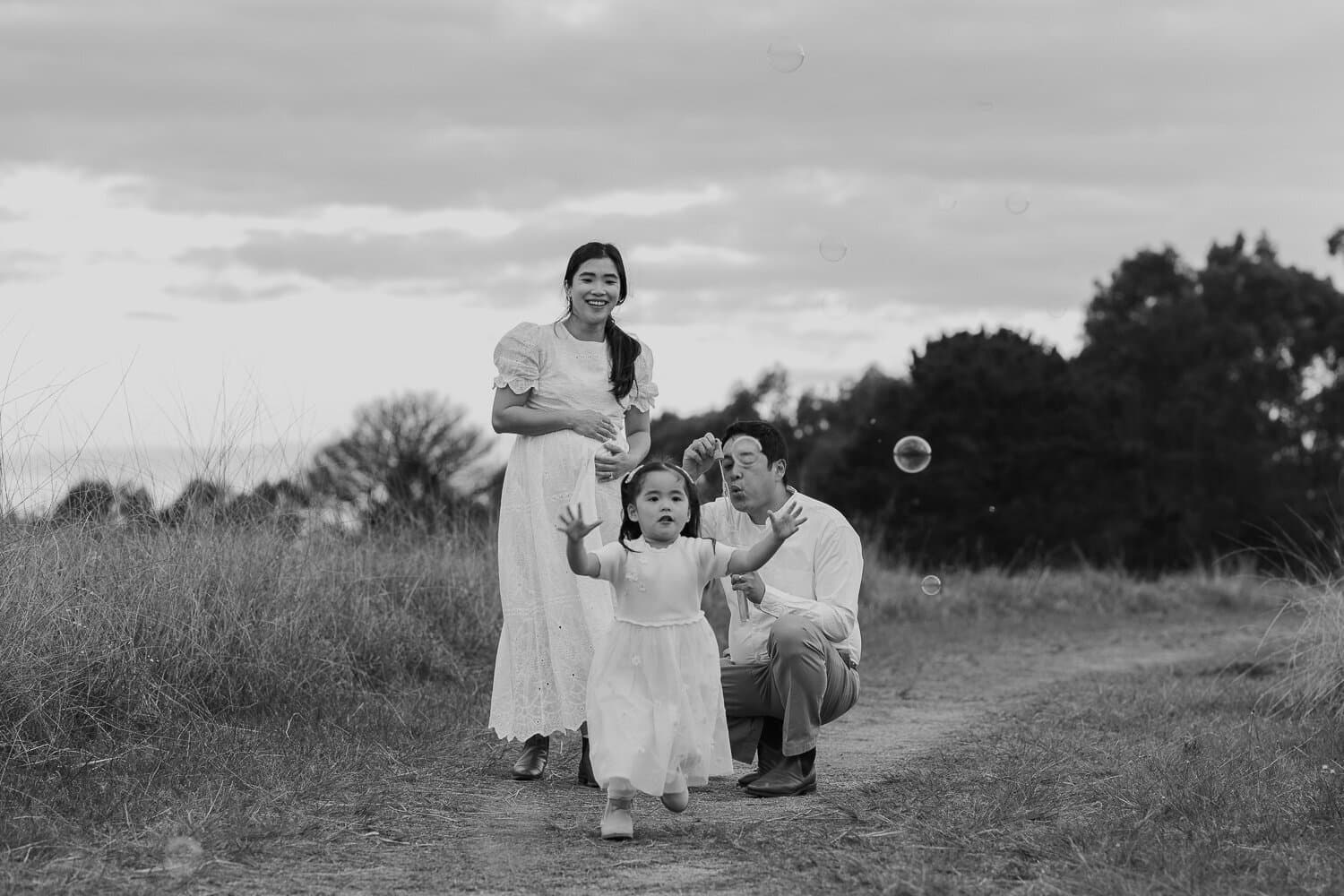 Black and white maternity photograph of a mother-to-be and her children blowing bubbles