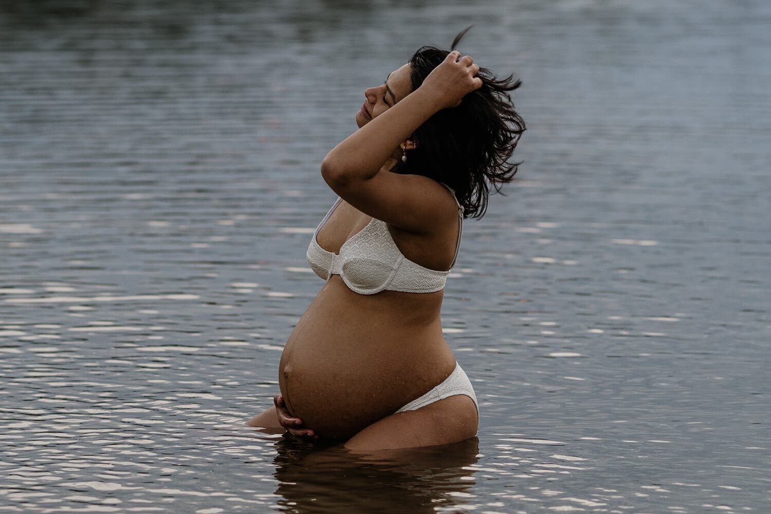 Mum-to-be running her hands through her hair in the water at sunrise