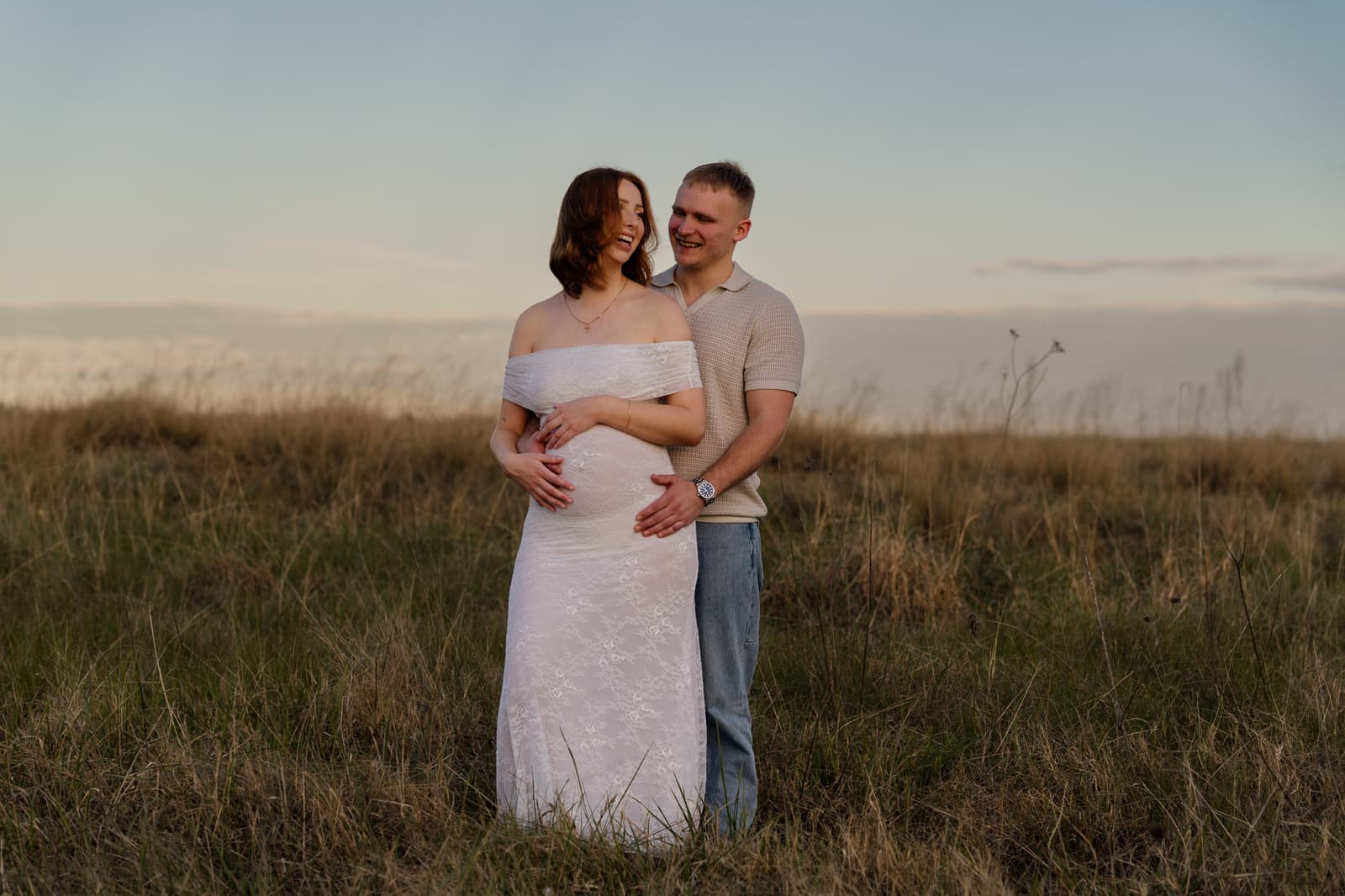 Expecting couple holding the bump together in a golden field at sunset