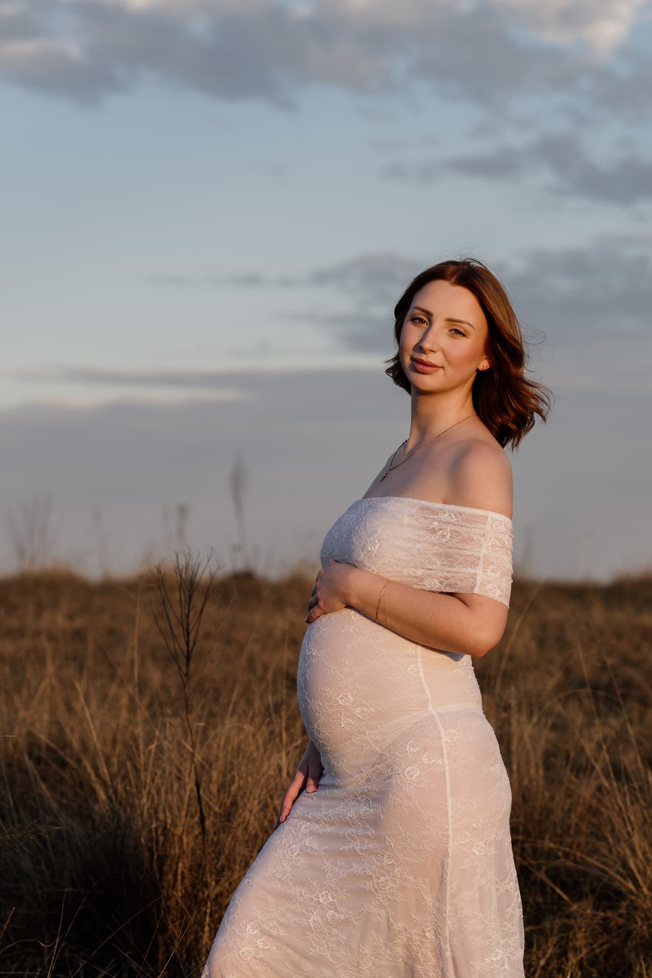 Mum-to-be in a flowing gown in long golden grass at dusk
