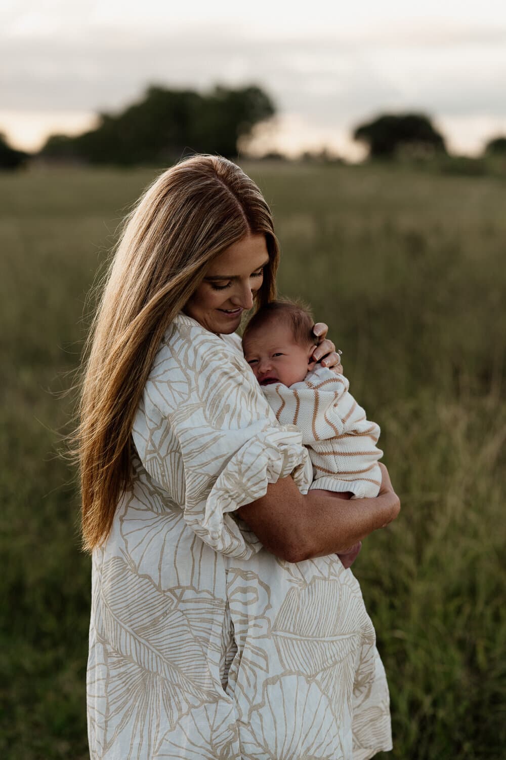 Mother cradling her newborn in long grass at sunset near Sydney