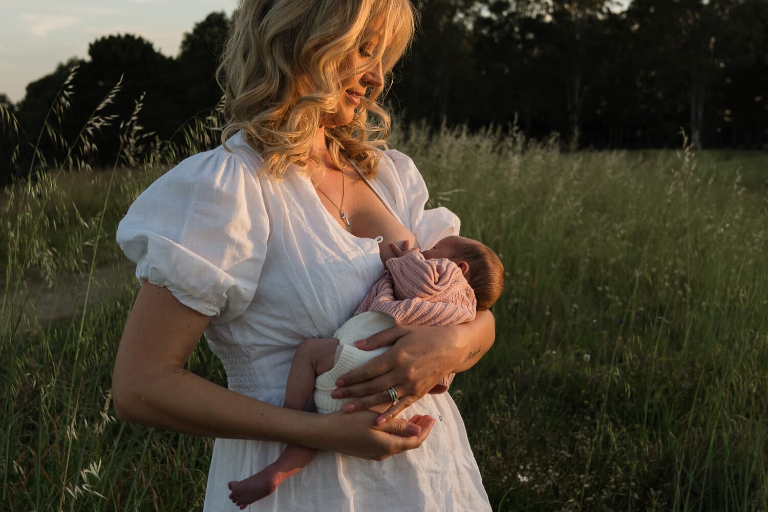 Mother holding her newborn in long grass at dusk