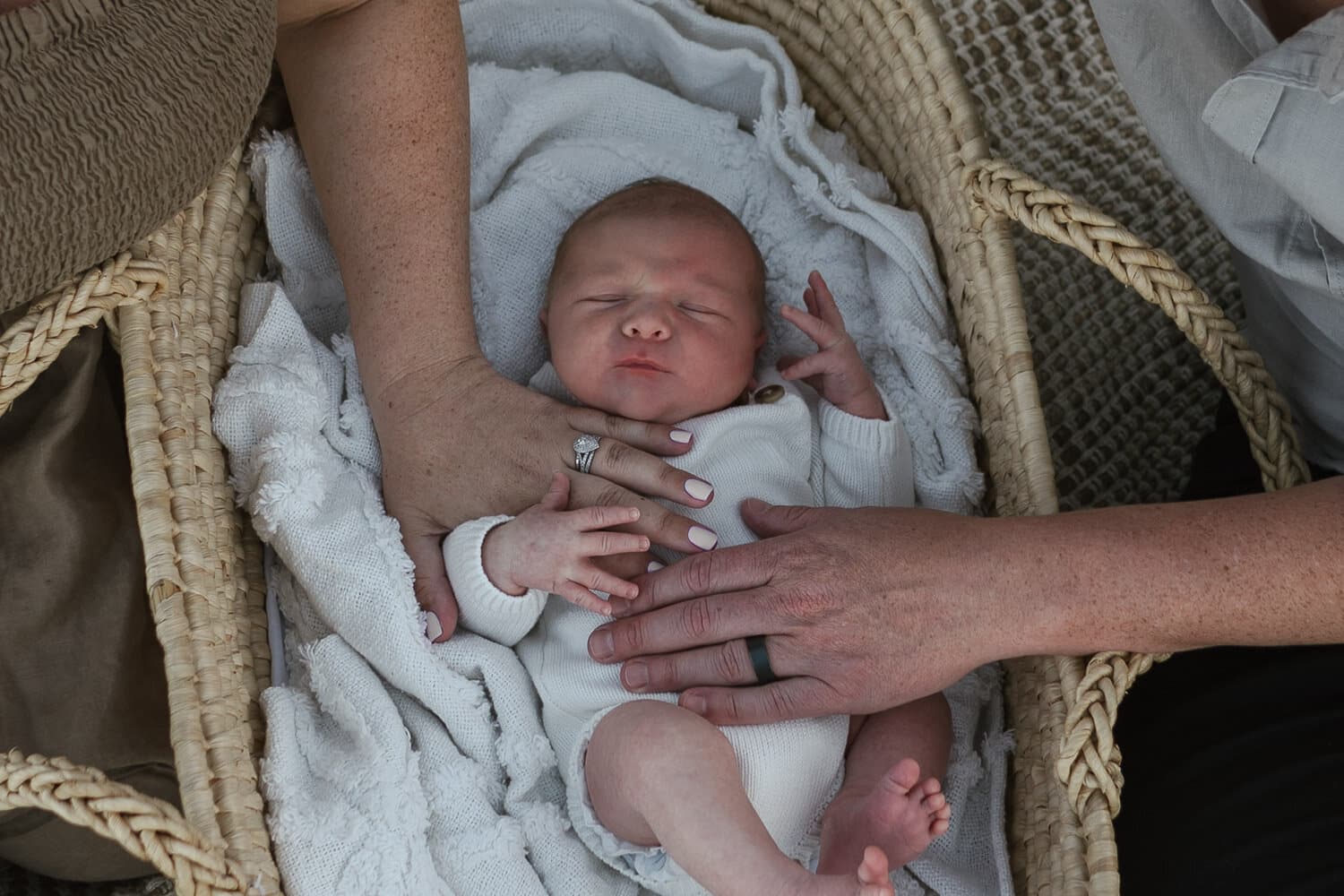 Newborn settled in a basket with a parent's hands nearby
