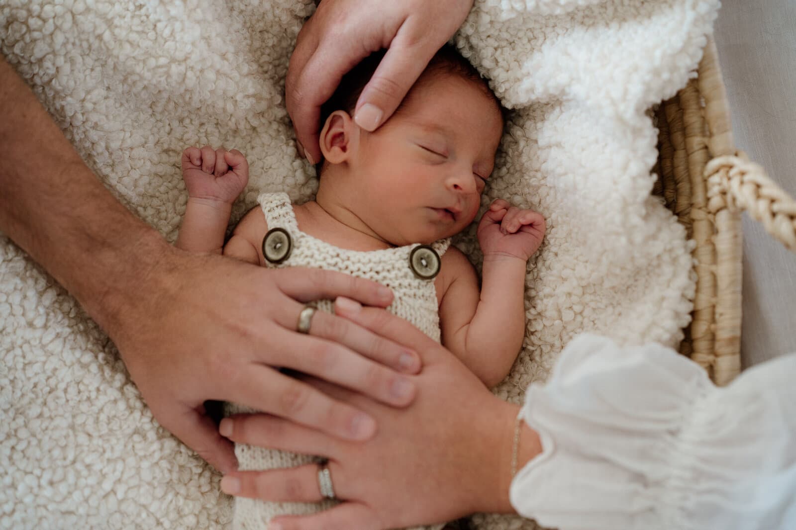 Newborn asleep in a basket with a parent's hands resting alongside