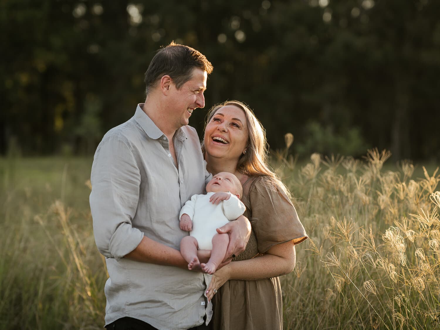 New parents laughing together holding their newborn in an open field