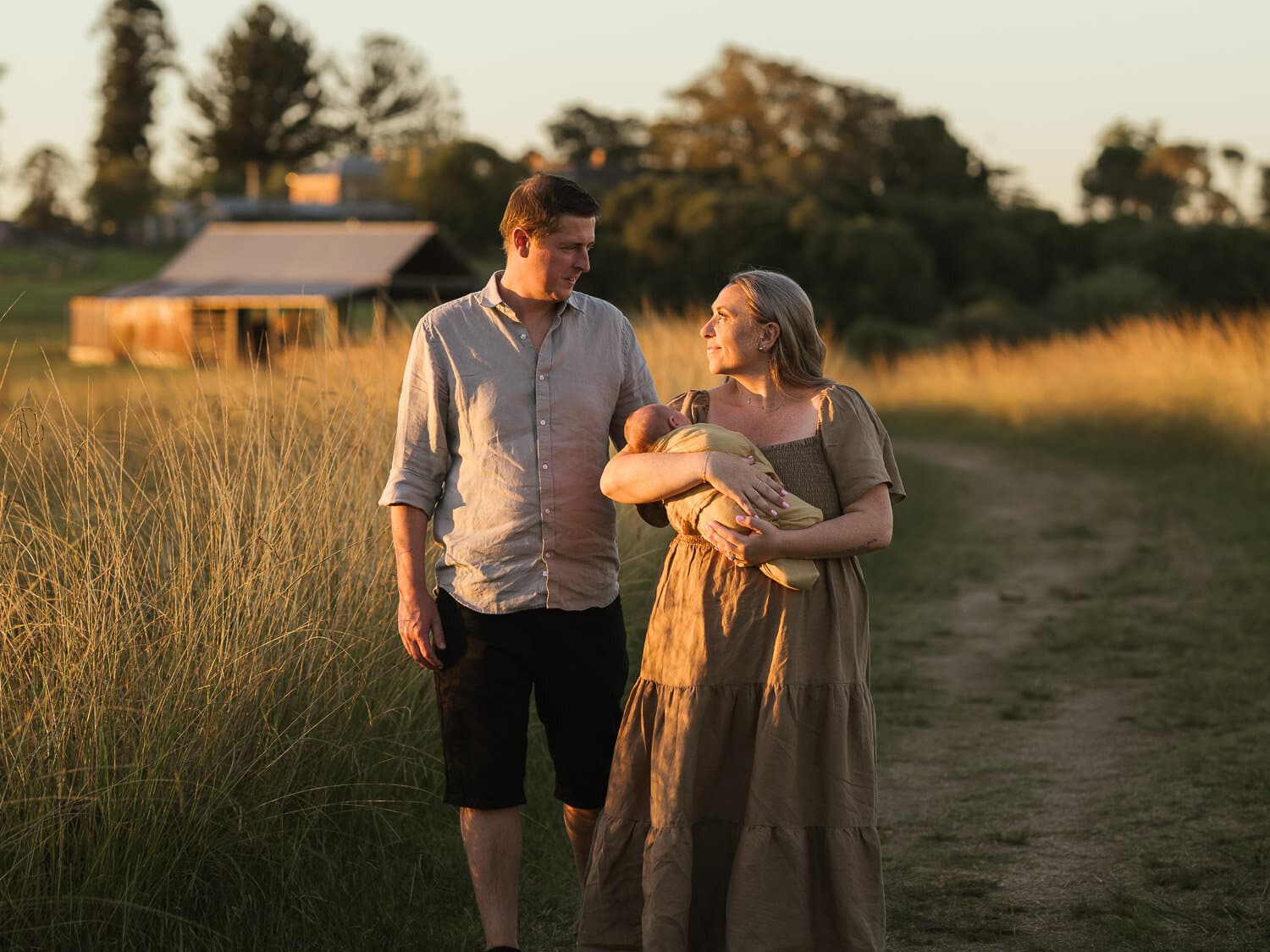 New parents holding their newborn in a Sydney field at golden hour