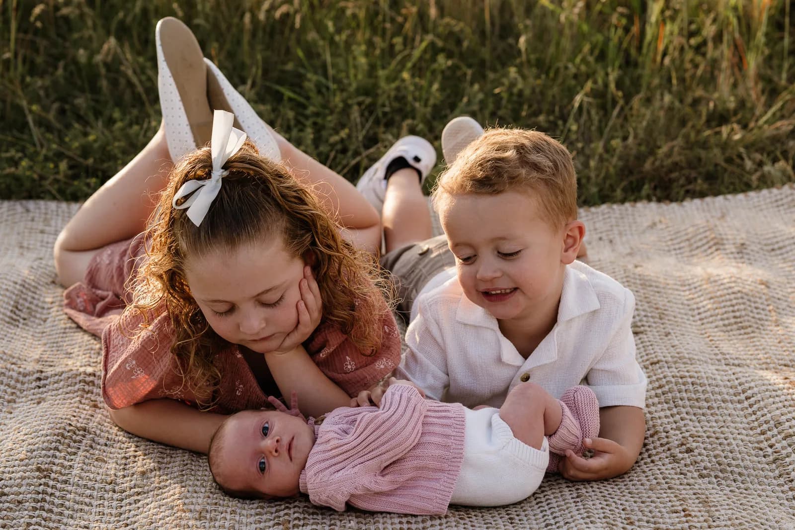 Older children lying on a rug beside their newborn sibling