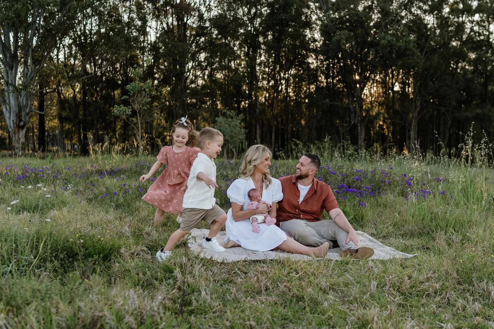 Family on a picnic rug in a paddock with their newborn