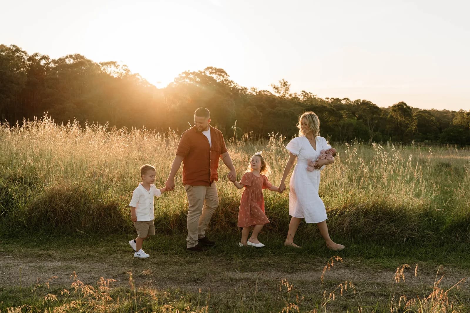 Family walking together through a paddock at sunset with their newborn