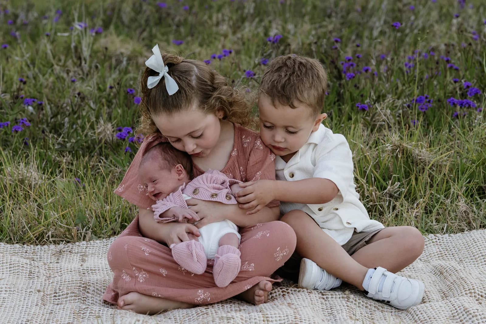 2 older children sitting with their newborn sibling on a rug