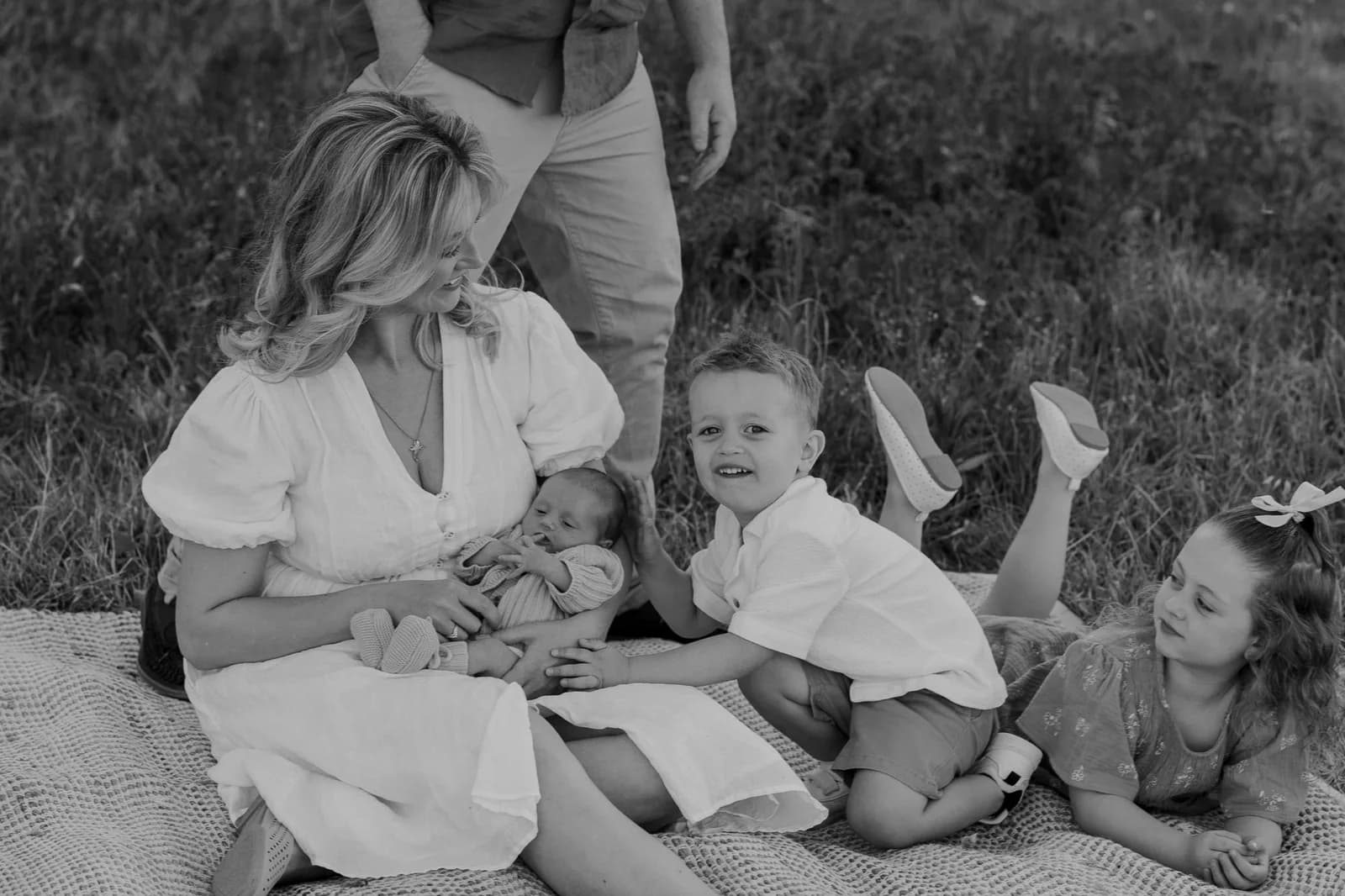 Black and white frame of a mother with her newborn and older children on the grass