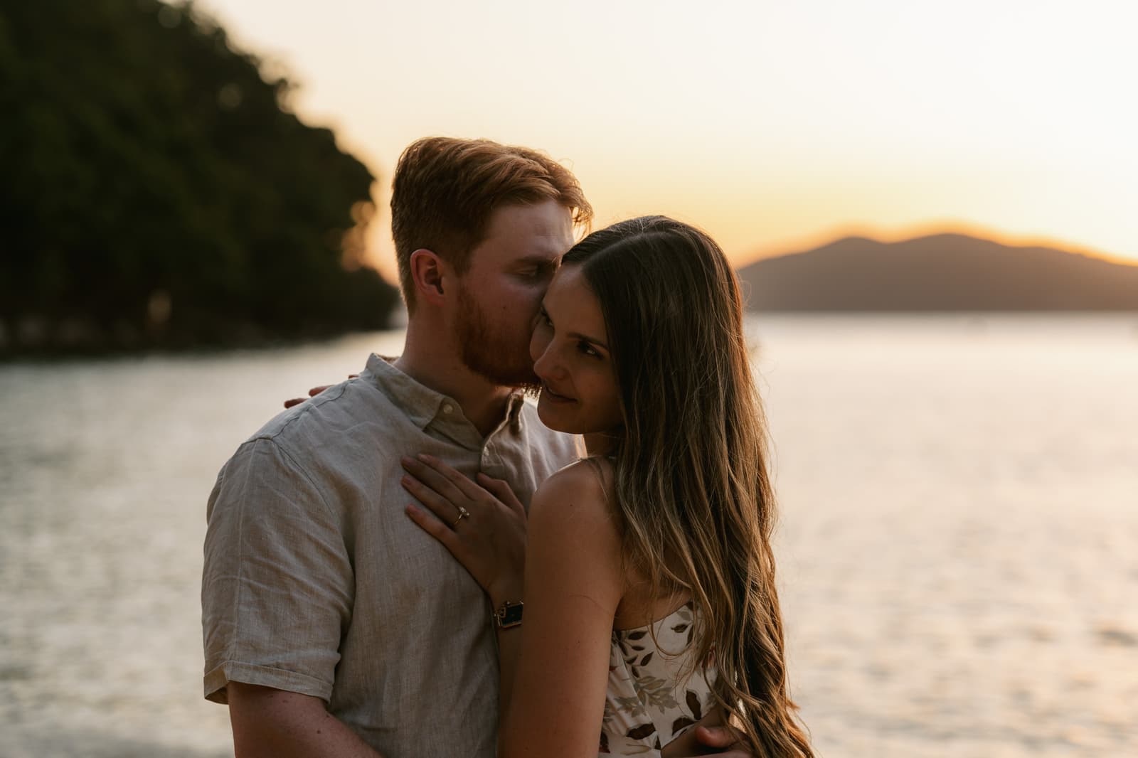 Newly engaged couple kissing beside the water at golden hour