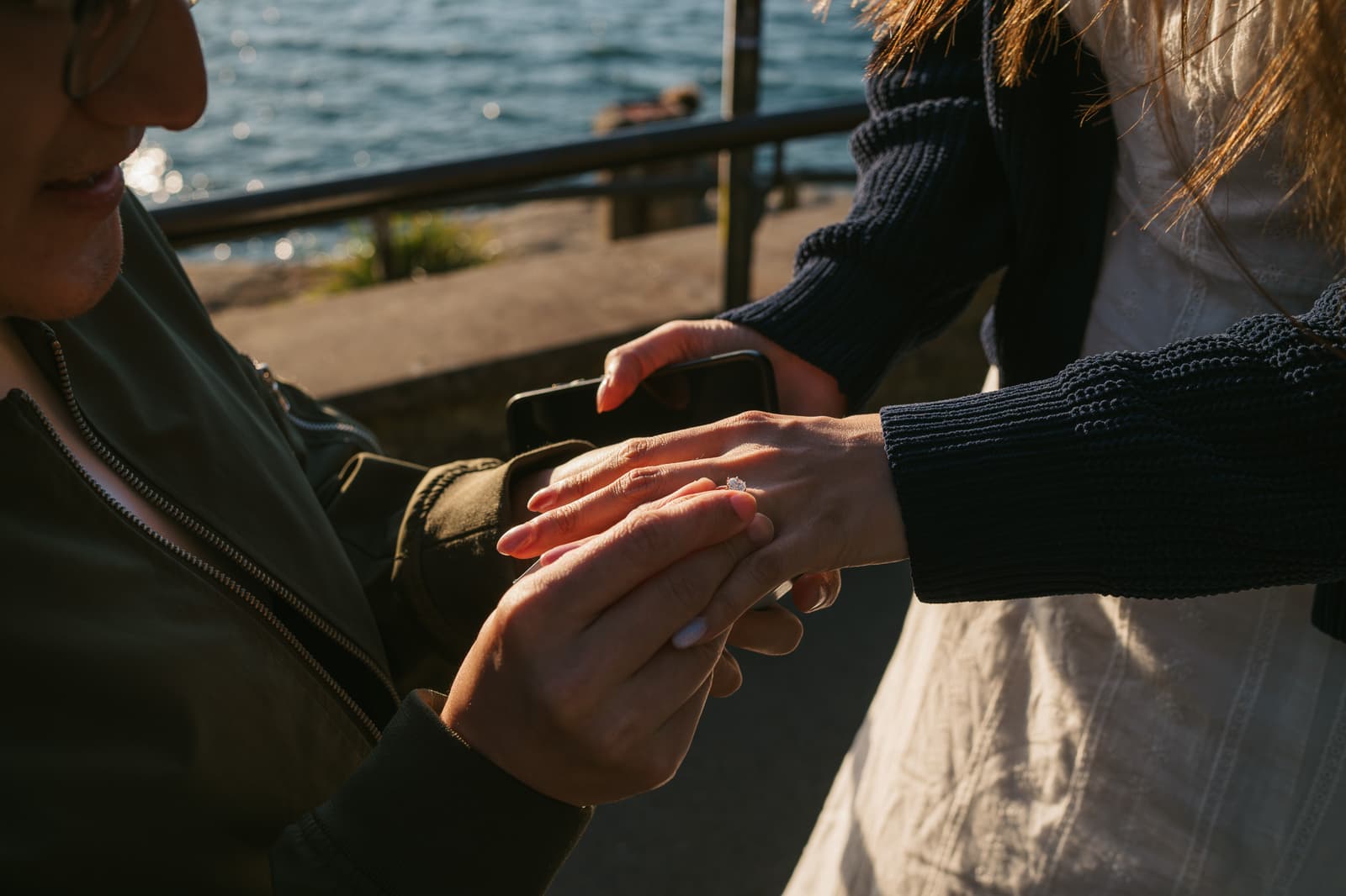Close-up of the engagement ring being placed on her finger by the harbour