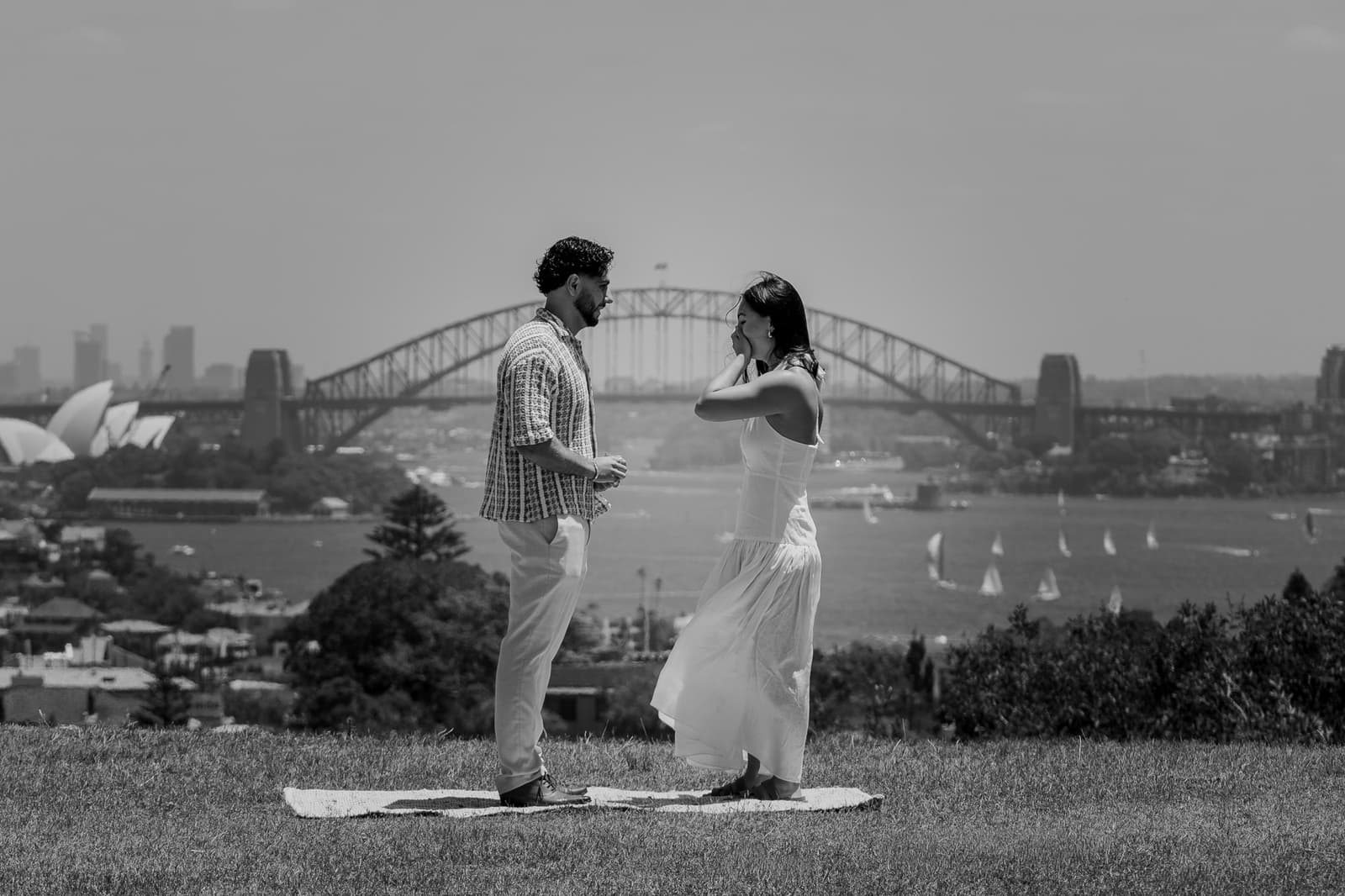 Black and white photograph of the proposal on the grass above Sydney Harbour
