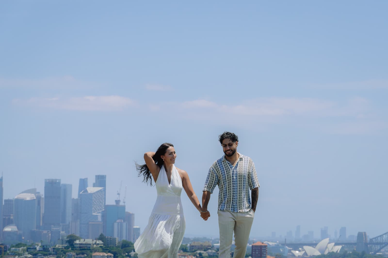 Couple walking hand in hand with the Sydney skyline behind them