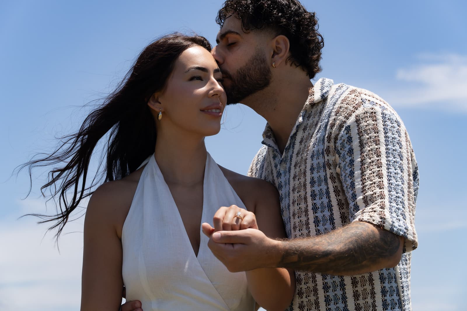 Newly engaged couple kissing as her hair catches the breeze