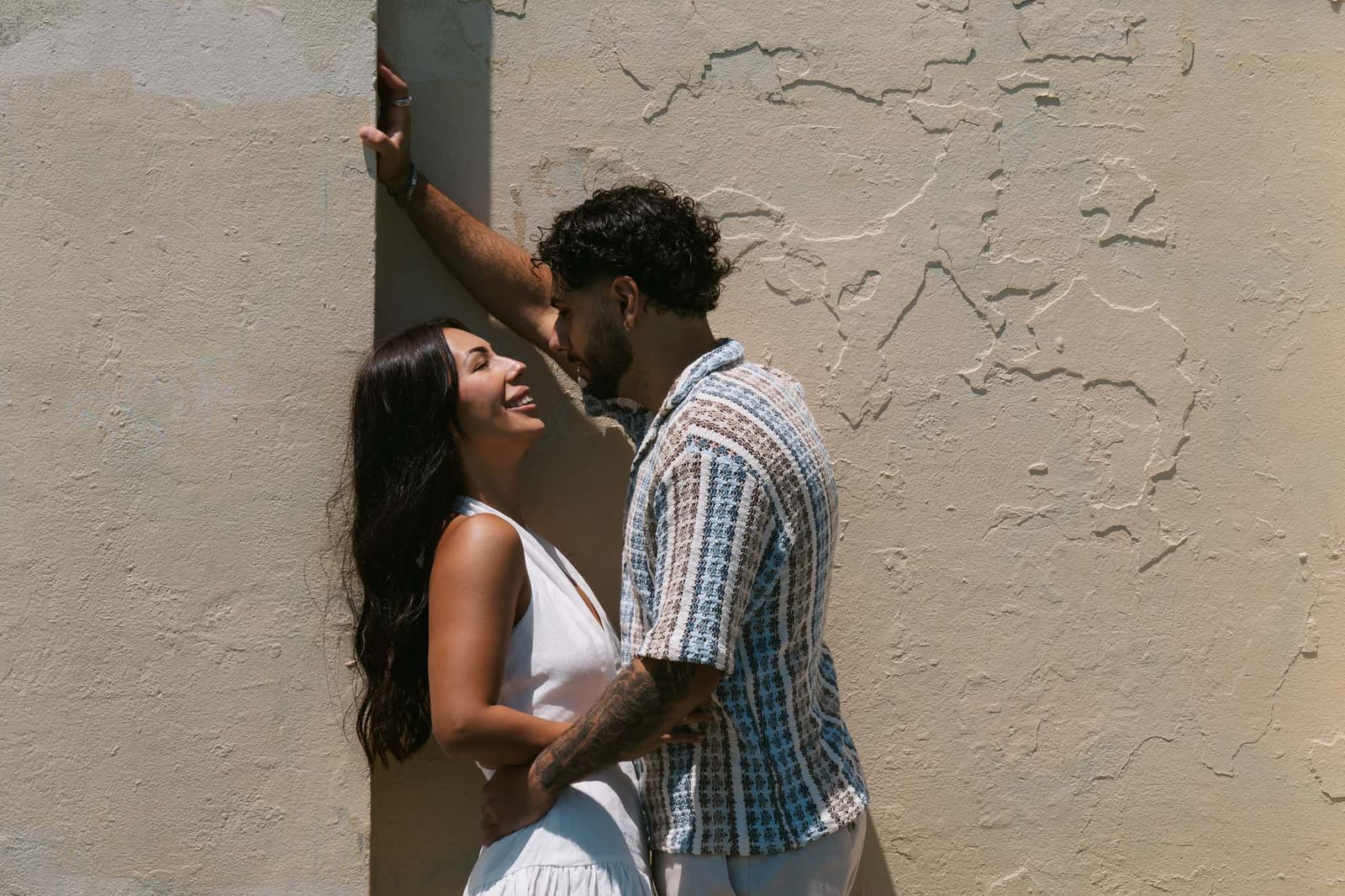 Newly engaged couple leaning against a sunlit wall