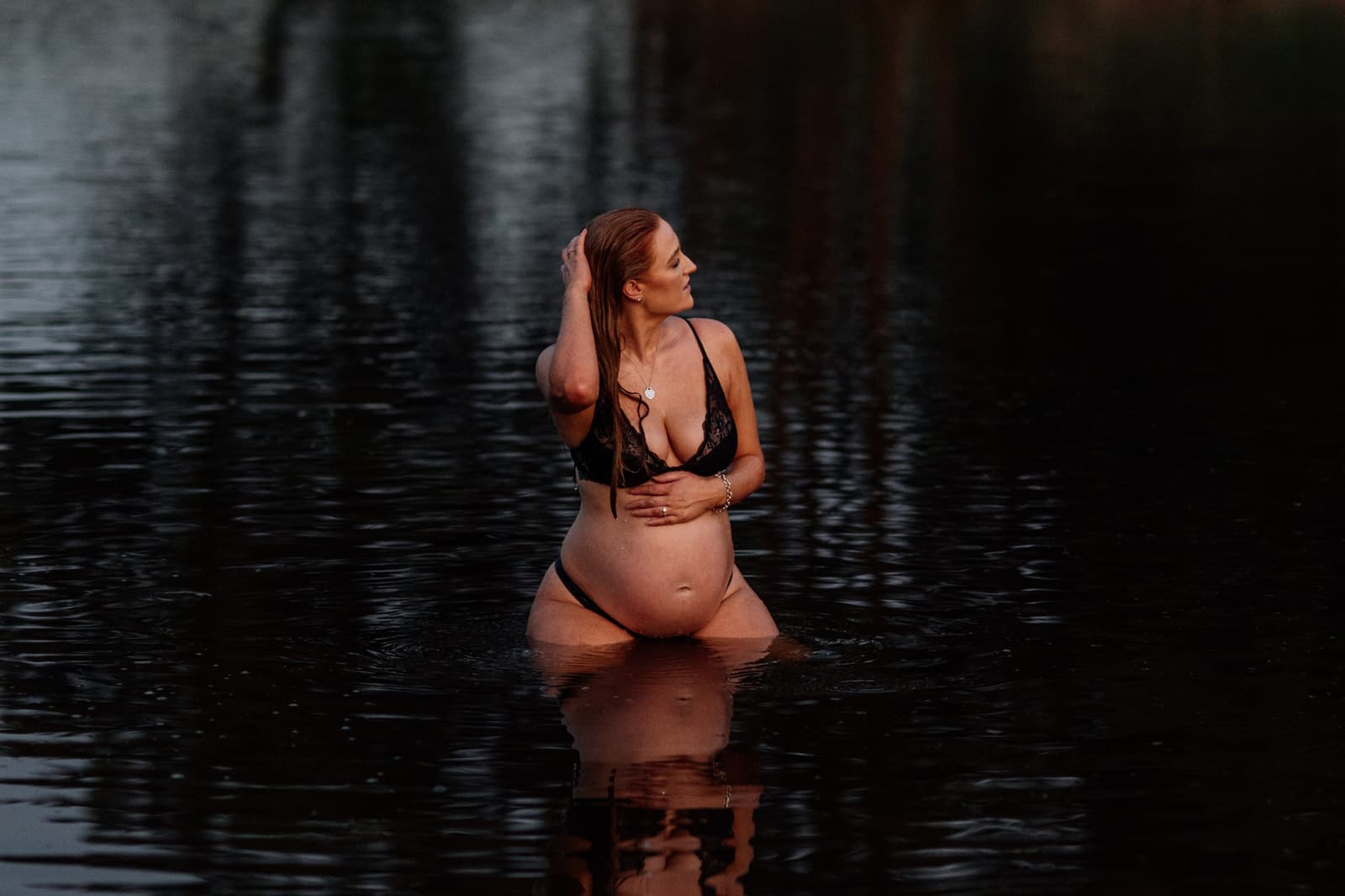 Expecting mother standing in still dark water at dusk during a maternity session