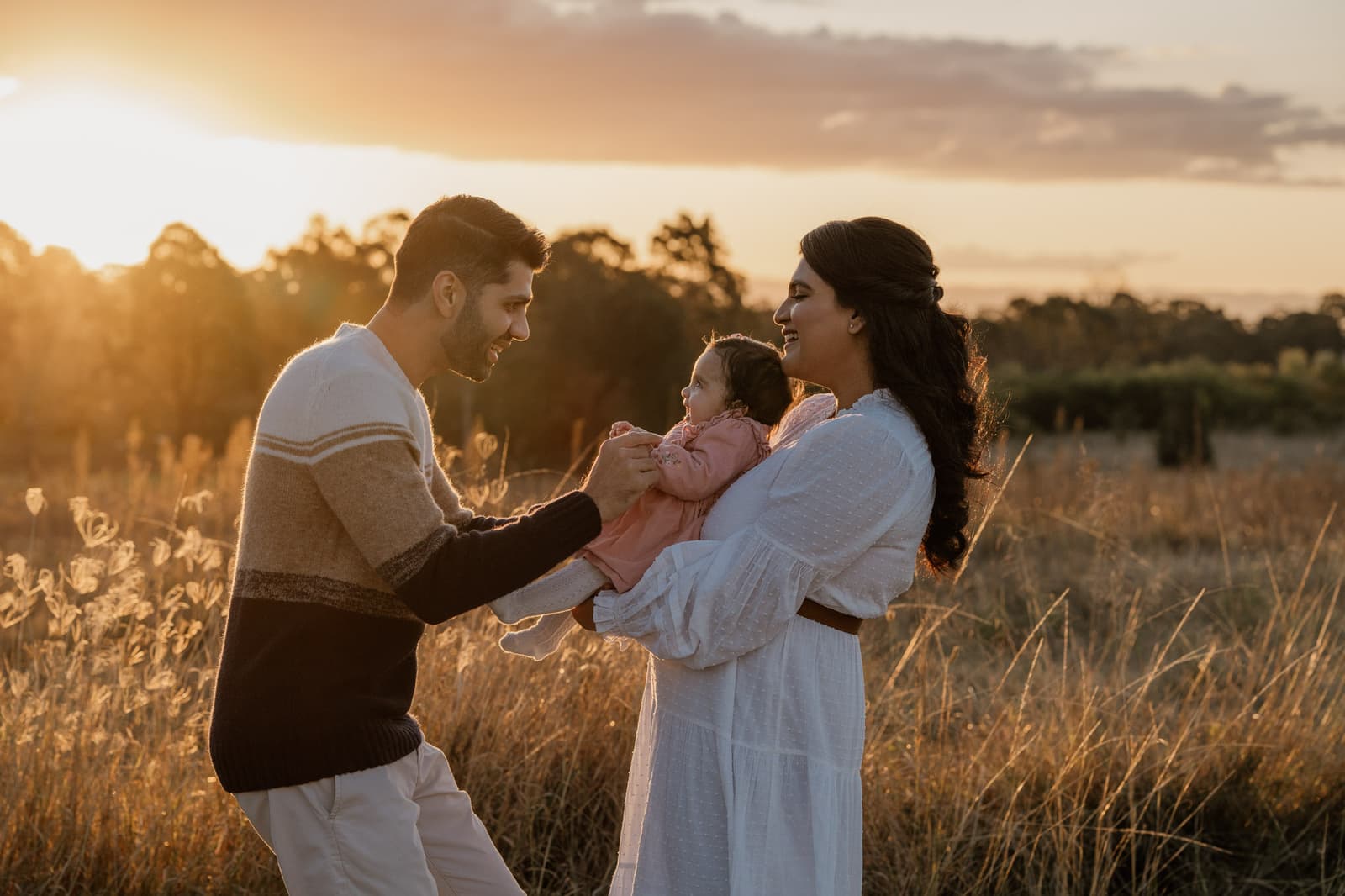 Parents holding their baby in a golden field at sunset during a Sydney family session